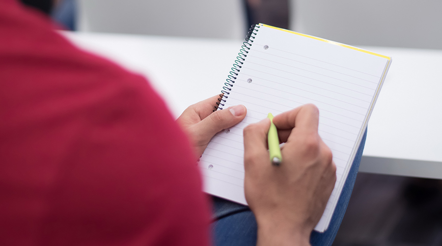 Alumno con pluma escribiendo en inglés en un cuaderno